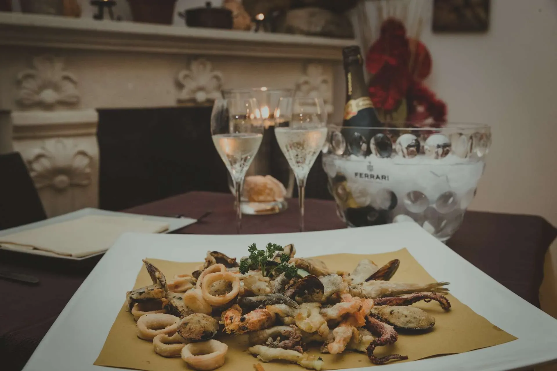 Frittura di mare servita in sala con calici e una bottiglia di Ferrari